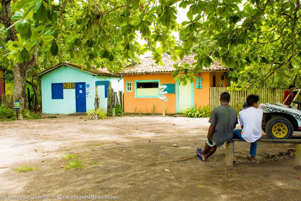 Imagem de meninos sentados em um banco e ao fundo casinhas coloridas em Caraiva.